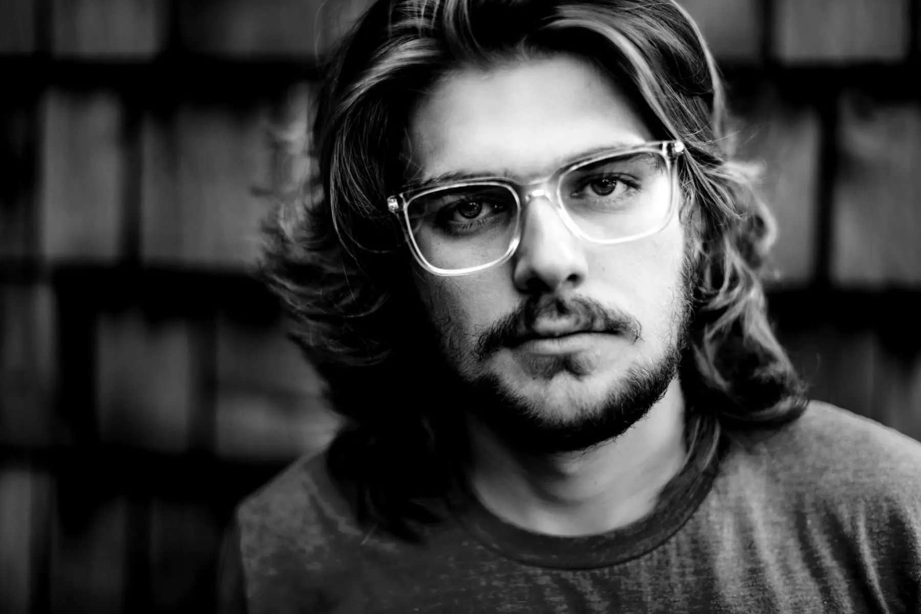 Jules — Portrait of a person with wavy shoulder-length hair, glasses and a light beard