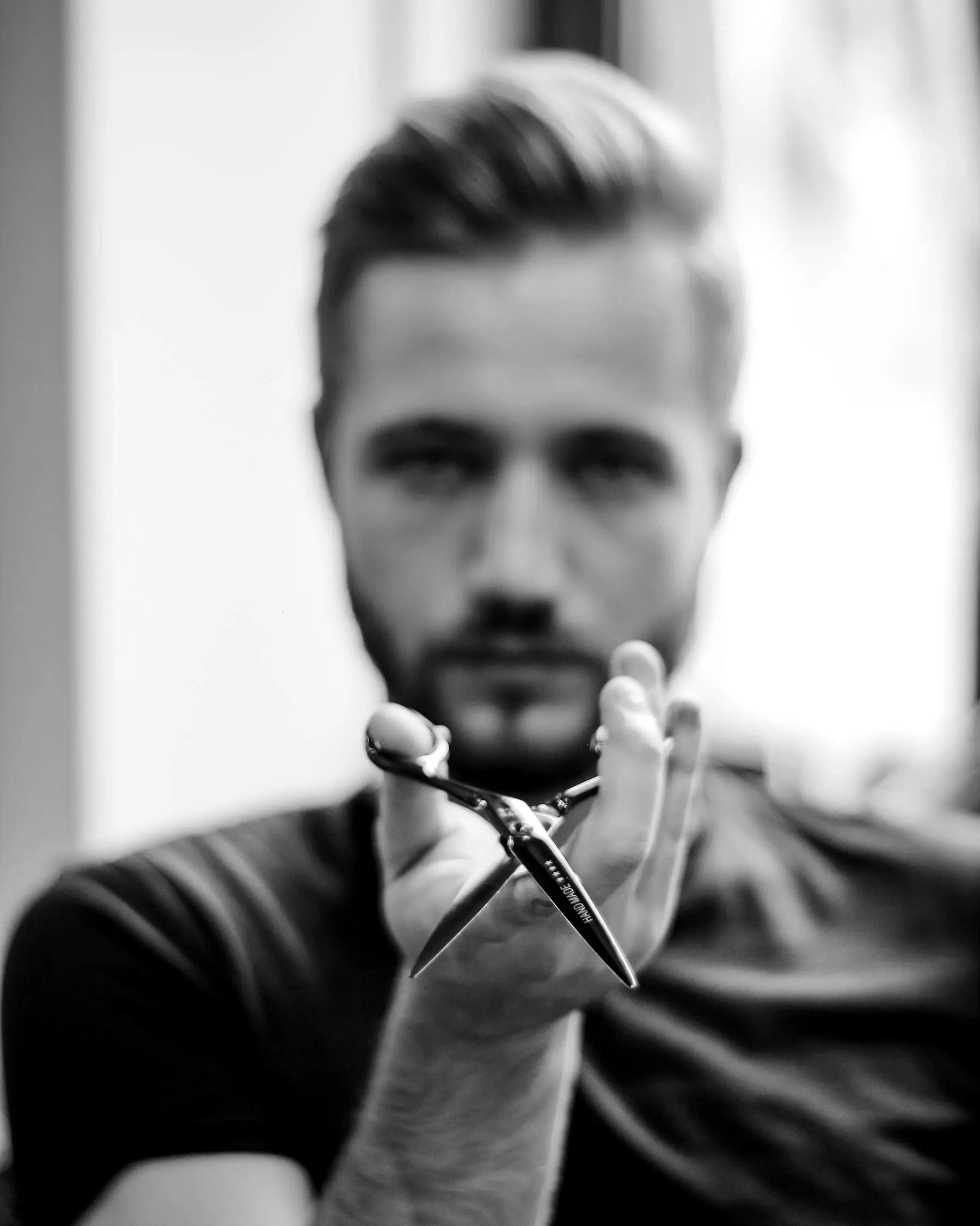 Milo — Portrait of a man with a short fade holding a pair of scissors up in front of him