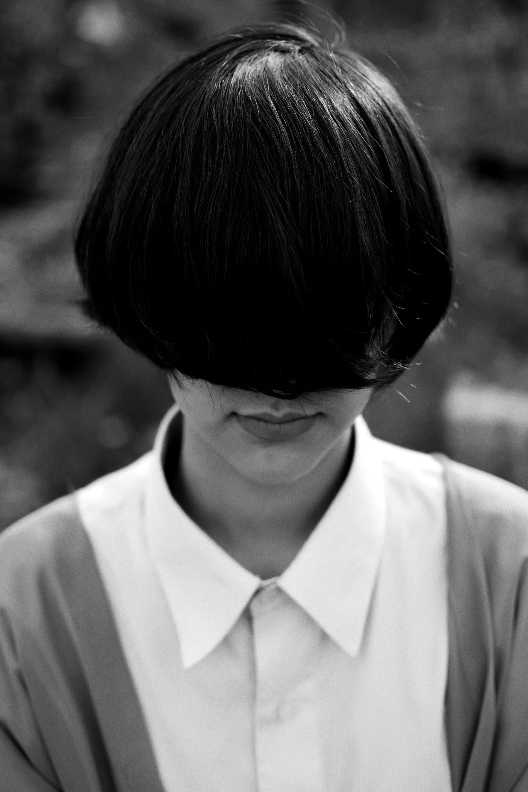 A person with a blunt bowl-shaped crop, hair falling over the face