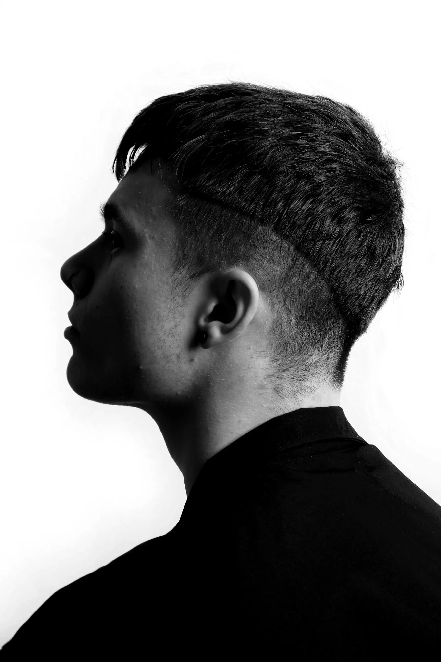 Side profile of a young man with a clean skin fade against a white wall