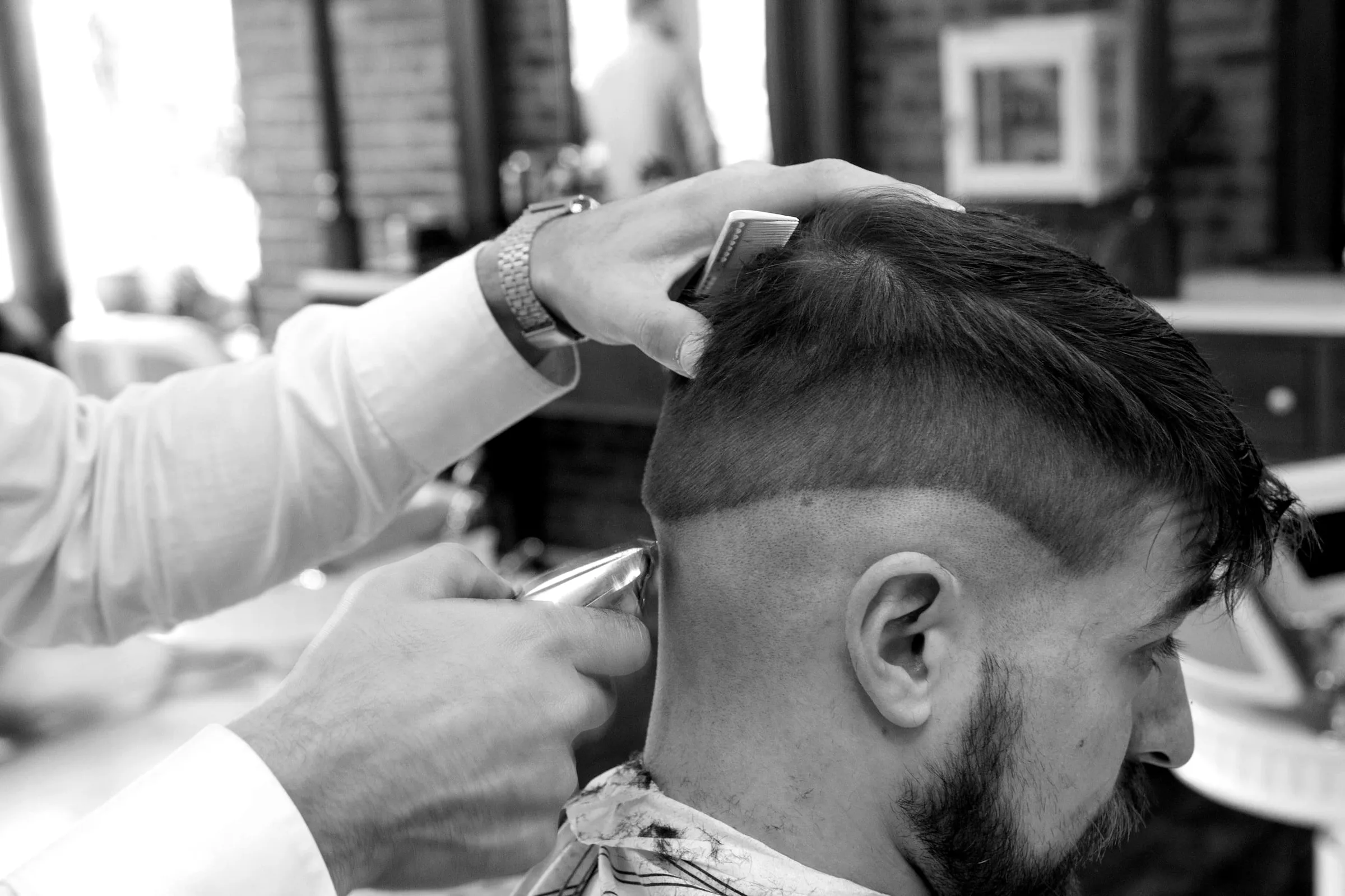 A barber's hands cutting the side of a client's hair with a razor, profile view