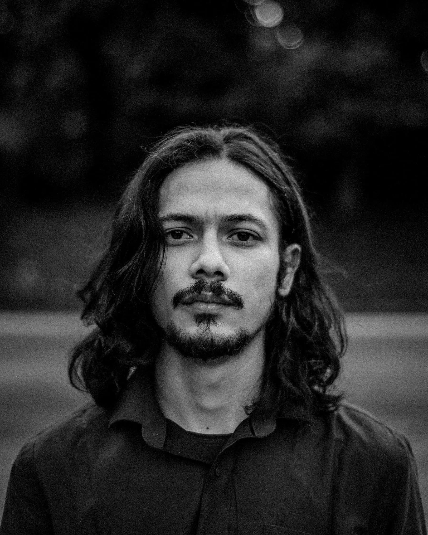 Front portrait of a man with long straight hair parted in the middle and a goatee
