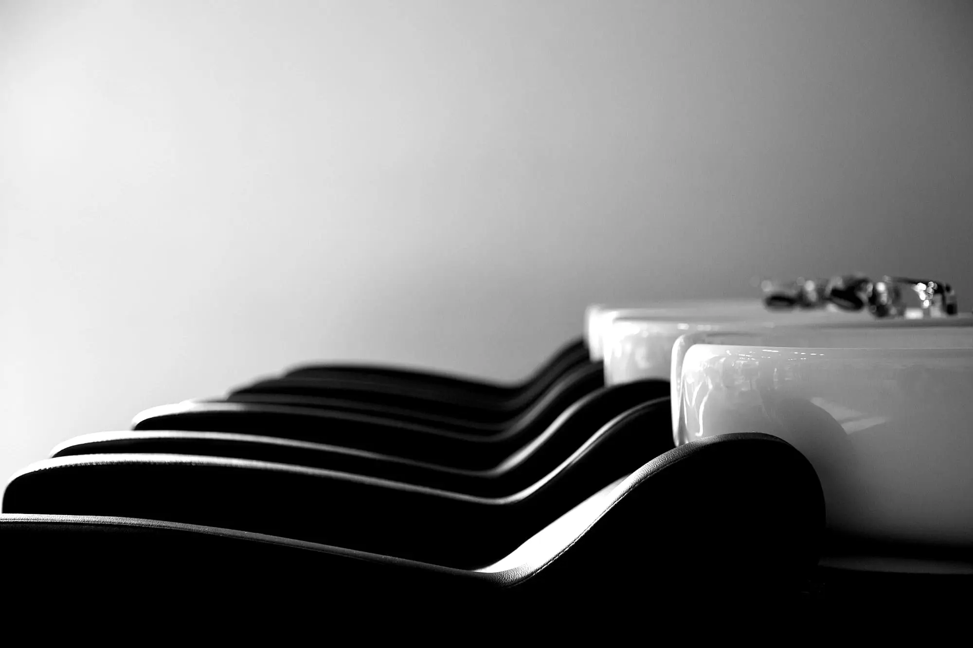 A row of black shampoo chairs with white basins against a bare wall