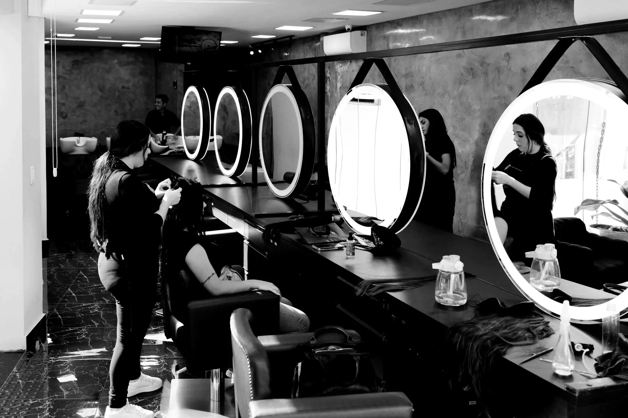 A row of round mirrors above the stations in a dark salon, a stylist working at one